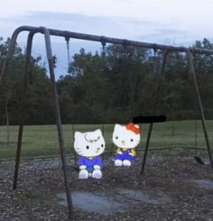 two hello kitty dolls sitting on swings in a park with trees and grass behind them