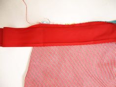 red and white checkered cloth with thread on it next to sewing needles, scissors and needle