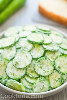 cucumber slices are arranged in a bowl on a table next to bread and green beans