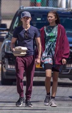 a young man and woman walking down the street holding hands with one another, both carrying pizza boxes