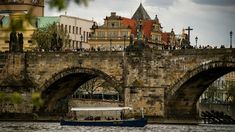 a boat on the water in front of an old bridge with people standing on it