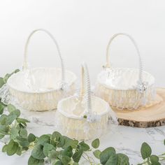 two white baskets sitting on top of a table next to green leaves and greenery