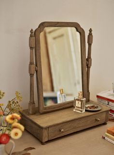 a wooden dressing table with a mirror and perfume bottle on the top, next to flowers