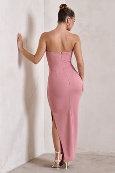 a woman in a pink dress leaning against a wall with her back to the camera