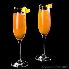 two champagne flutes filled with orange juice and topped with lemon wedges on a black background