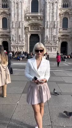 a woman standing in front of a building with pigeons on the ground and people walking around