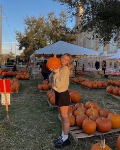 a woman holding a pumpkin in front of a large group of pumpkins on display