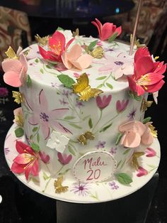 a white cake with pink and yellow flowers on it's side, decorated with gold leaves