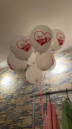 white balloons with red hearts on them are hanging from the ceiling in front of a stone wall