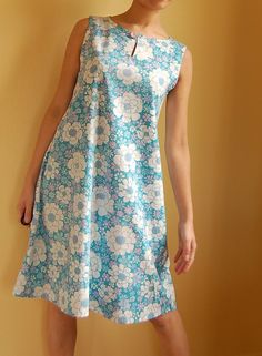 a woman standing in front of a yellow wall wearing a blue and white floral dress