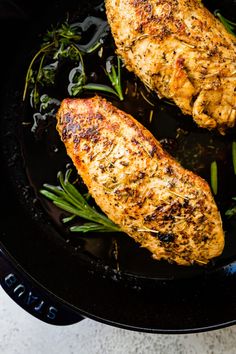 two pieces of chicken in a skillet with green beans and rosemary on the side