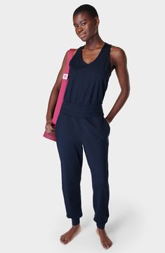 Perfect for low-impact studio workouts or just lounging around, this sporty jumpsuit is made from easy-moving stretch fabric with sweat-wicking properties. The relaxed fit is detailed with a keyhole racerback for added breathability. 60" length; 29" inseam; 10" leg opening (size Medium) Back keyhole with button-and-loop closure V-neck Sleeveless, with cutaway shoulders Front slant pockets Elastic waist Banded cuffs Moisture-wicking fabric engineered for dryness and comfort 85% polyester, 15% ela Womens Summer Jumpsuits, Black Women Dress, Long Pant Jumpsuit, Yoga Jumpsuit, Jumpsuit Navy Blue, Yoga Outfits, Maternity Swimwear, Sweaty Betty, Womens Activewear