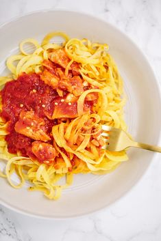 a white bowl filled with pasta and sauce on top of a marble countertop next to a silver fork