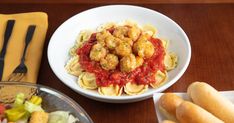 pasta with shrimp and sauce in a bowl next to breadsticks on a table