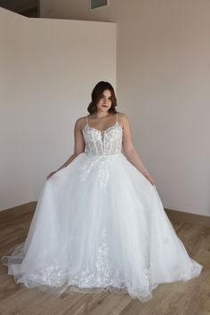 a woman in a white wedding dress standing on a wooden floor with her hands on her hips