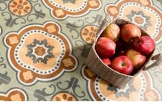 a basket filled with red apples sitting on top of a tiled floor covered in orange and white designs