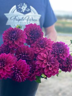 a person holding a black vase filled with purple flowers