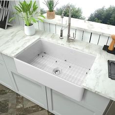 a white kitchen sink sitting on top of a counter next to a potted plant