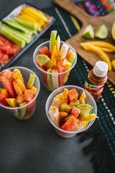 three plastic cups filled with fruit sitting on top of a table next to other fruits