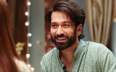 a man with a beard smiling and looking at the camera in front of a mirror