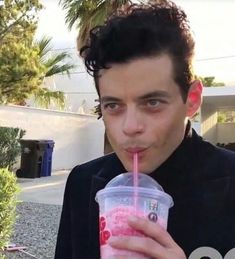 a young man drinking a pink drink from a plastic cup with a straw in his mouth