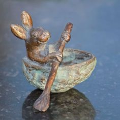 a bronze figurine sitting in a bowl holding a wooden stick