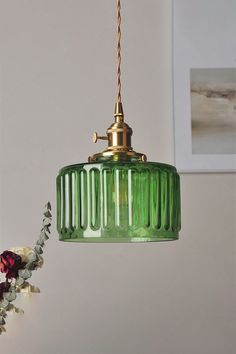 a green glass light hanging from a gold colored ceiling fixture with flowers in the foreground