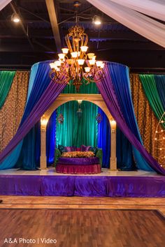 a stage set up for a wedding with blue and green drapes, chandelier, and flowers