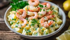 a bowl filled with pasta and shrimp on top of a wooden table next to lemon wedges