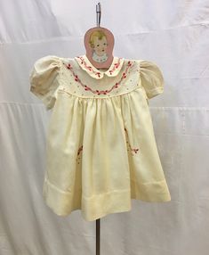 "1940s, 18\" chest, ecru wool shammy  baby dress , 2 years, with red embroidery around collar. Yoke, and faux pockets at hip level.   Dress has cap sleeves, and a Peter pan collar.  Dress is fastened in back with 2 mother of pearl buttons.  Measurements: chest 18\" Shoulder to shoulder  8\" Shoulder to hem  13\" Neck opening 8\" Sleeves 4\" Width at bottom 42\" Condition excellent" Embroidered Cotton Dress With Peter Pan Collar, Vintage Cream Embroidered Dress, Cream Vintage Embroidered Dress, Vintage Cream Dress With Doll Collar, Cream Fitted Dress With Peter Pan Collar, Vintage Smock Dress With Short Sleeves, Vintage Short Sleeve Smock Dress, Pan Collar Dress, Vintage Childrens Clothing