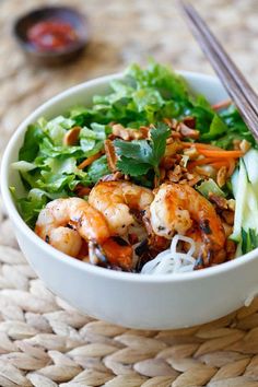 a white bowl filled with salad and shrimp on top of a woven place mat next to chopsticks