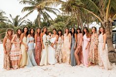 a group of women standing next to each other on top of a sandy beach with palm trees