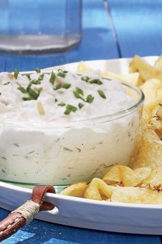 a white plate topped with a bowl of dip next to chips