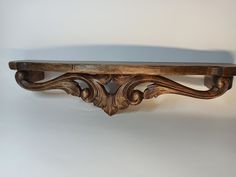 an antique wooden shelf with ornate carvings on the top and bottom, against a white wall