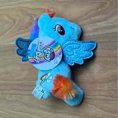 a blue stuffed animal with an orange tail and wings on a wooden floor next to a tag that says hello kitty