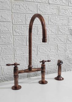 two faucets are shown in front of a white brick wall, one is copper and the other is black