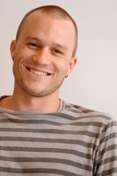 a man with a bald head smiling at the camera while wearing a gray and black striped shirt