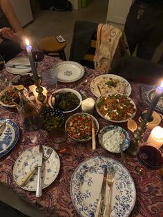 a table topped with plates filled with food next to a lit candle and two candles