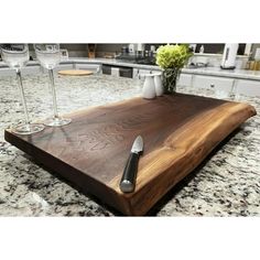 a wooden cutting board sitting on top of a counter next to two wine glasses and a knife