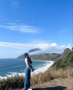 a woman standing on top of a hill next to the ocean