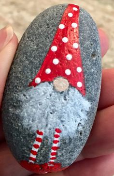 a hand holding a rock with a gnome painted on it's face and wearing a red hat