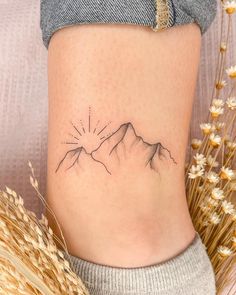 a small tattoo on the side of a woman's stomach, with mountains in the background