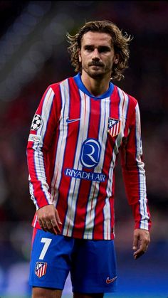 a man with long hair wearing a red and blue striped soccer uniform standing on a field