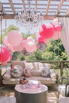 pink and silver balloons are hanging from the ceiling above a couch with pillows on it