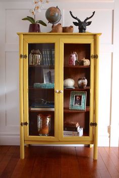 a yellow cabinet with books and vases on top