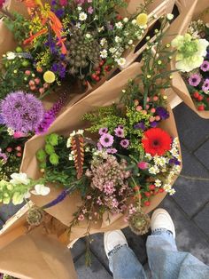 a person standing next to a bunch of flowers on top of a sidewalk with their feet in the air