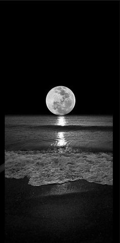 the moon is shining brightly over the water at the beach in black and white photo