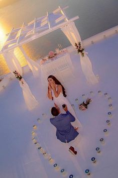 a man kneeling down next to a woman on top of a white bed covered in flowers