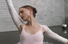 a woman in a white leotard is stretching her arms up with one hand