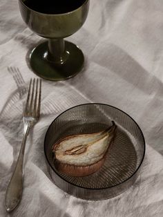 an apple slice on a glass plate next to a silver fork and cup with liquid in it